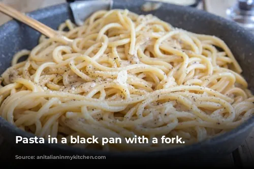 Pasta in a black pan with a fork.