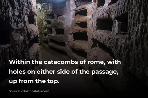 Within the catacombs of rome, with various holes on either side of the passage, lit up from the top.