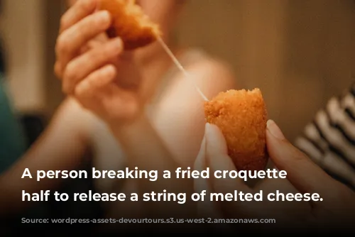 A person breaking a fried croquette in half to release a string of melted cheese.