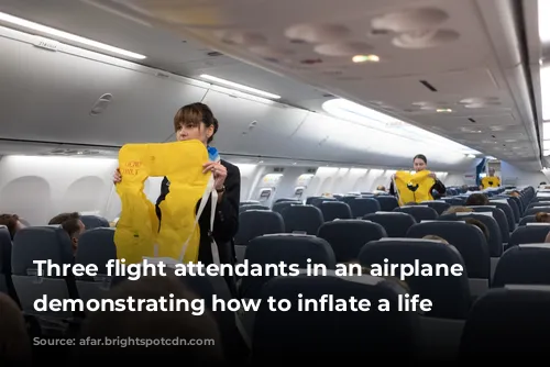 Three flight attendants in an airplane aisle demonstrating how to inflate a life vest