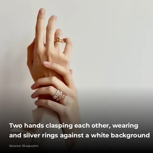 Two hands clasping each other, wearing gold and silver rings against a white background 