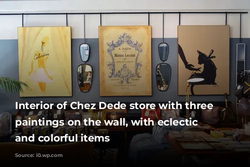 Interior of Chez Dede store with three large paintings on the wall, with eclectic furniture and colorful items 