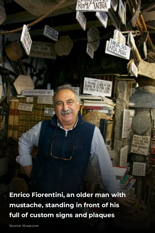 Enrico Fiorentini, an older man with a mustache, standing in front of his shop full of custom signs and plaques 